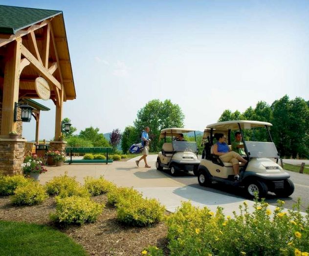 The image shows a couple of golf carts parked near a building with people around, surrounded by greenery and flowers.