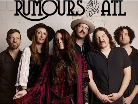 A band called Rumours Abl poses in front of a wall with their name, wearing dark and vintage-inspired outfits.