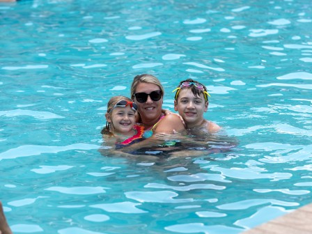 A woman with two children enjoy swimming in a pool together during a sunny day.