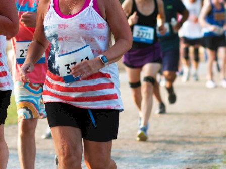 Participants in a marathon or running race, wearing numbered bibs and athletic clothing, running on a dirt path.
