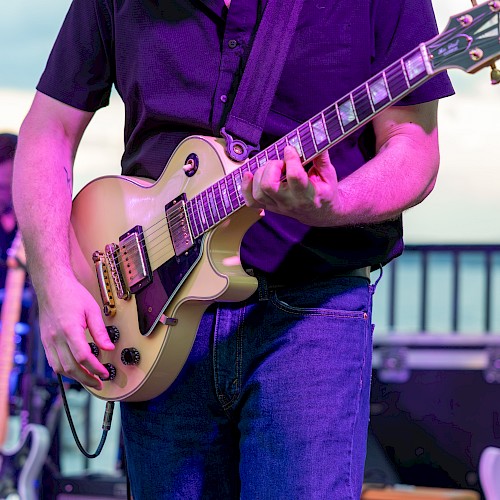 A person playing an electric guitar on stage during a live music performance outdoors.