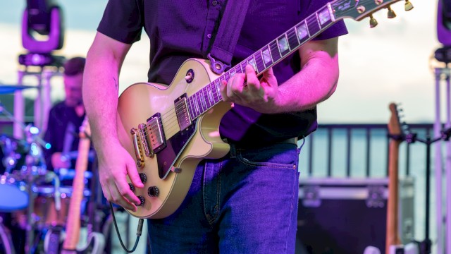 A person playing an electric guitar on stage during a live music performance outdoors.