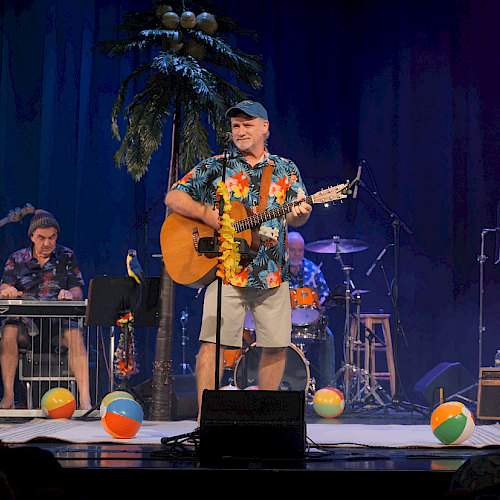 A group of musicians performing on stage with tropical decorations and beach balls, creating a lively, summer-themed atmosphere.