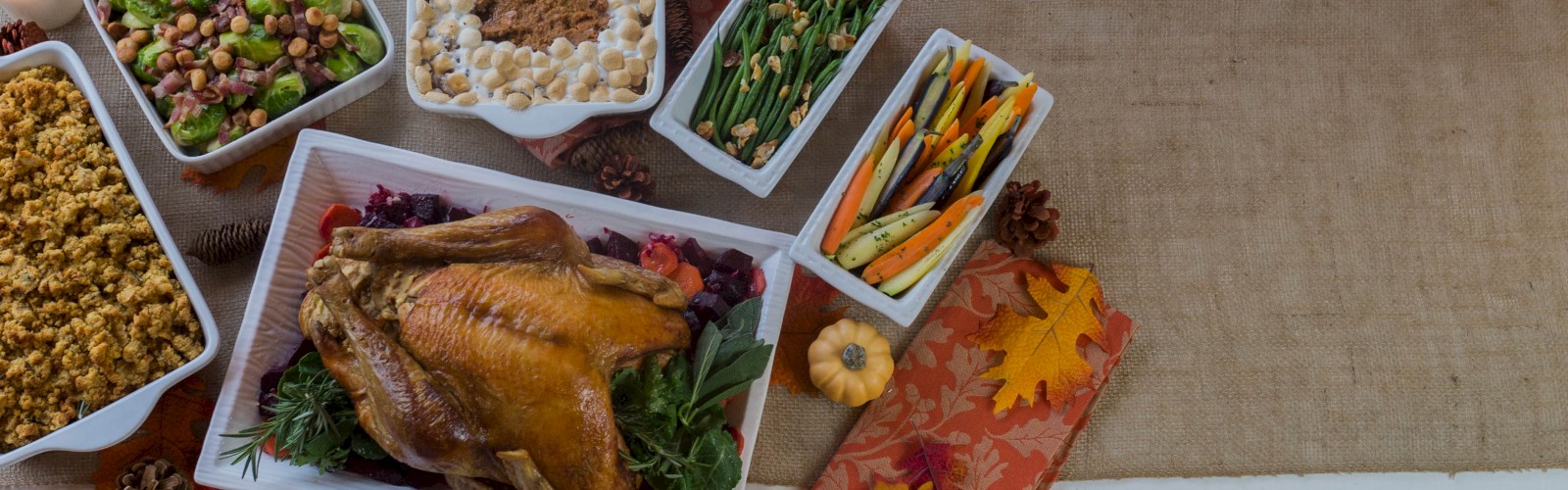 A Thanksgiving spread with roast turkey, stuffing, mixed beans, green beans, carrots, and a sweet potato casserole topped with marshmallows.