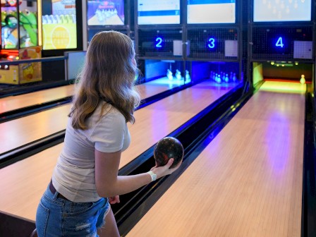 A person is bowling in an alley with neon lights as the ball is about to be released towards the pins.