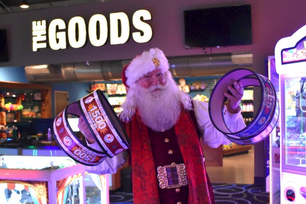 A person dressed as Santa is holding large ticket rolls in an arcade, with a sign reading 