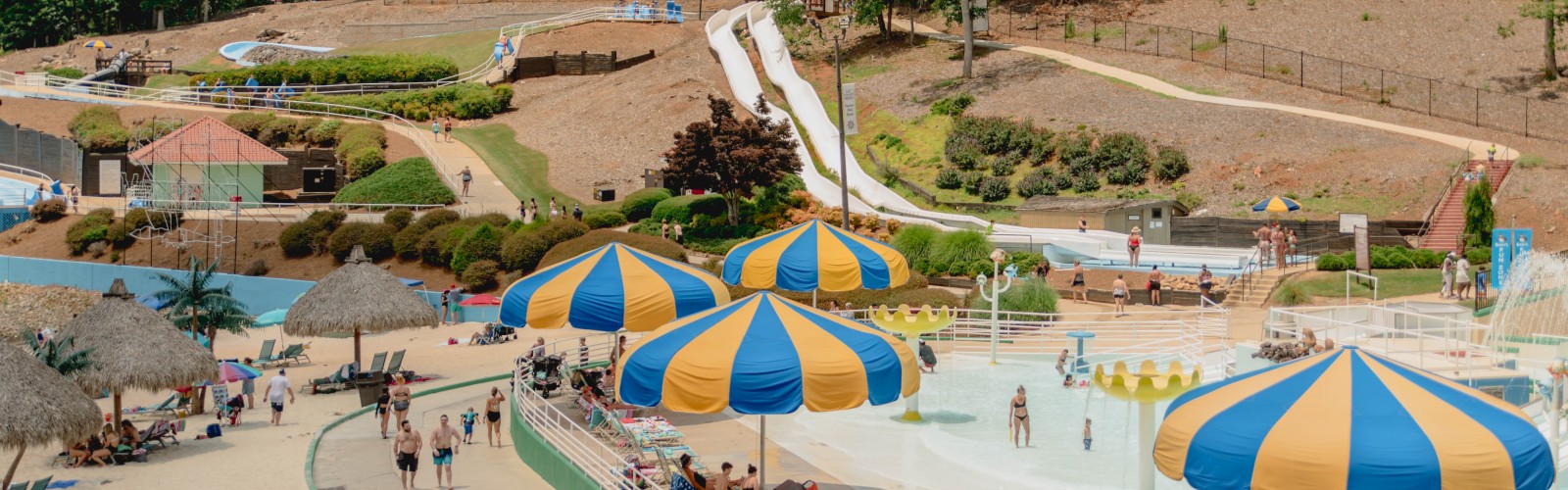 A water park with colorful umbrellas, slides, and pools is bustling with visitors enjoying the sunny day.