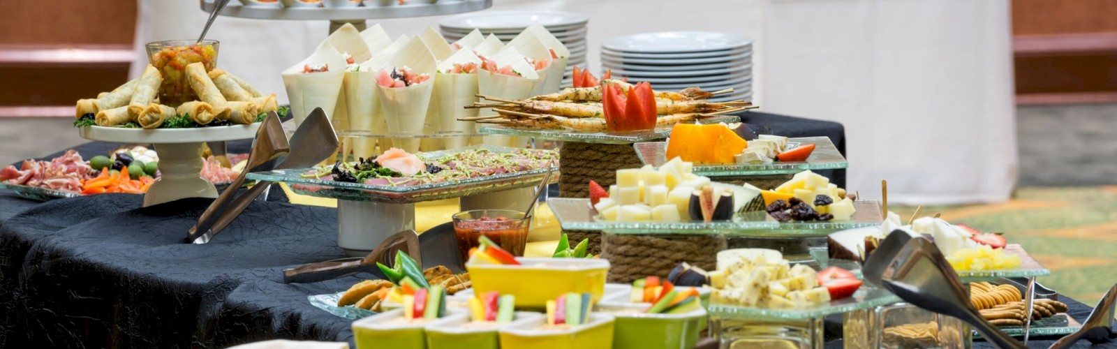 A buffet table with assorted appetizers, cheeses, fruits, and bread arranged elegantly on various platters and trays.
