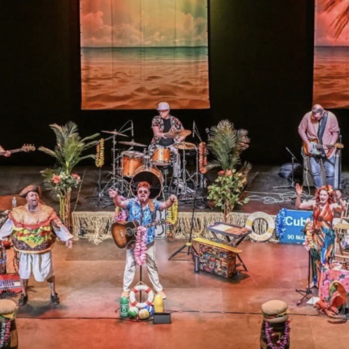 A vibrant stage performance with musicians and performers set against a tropical backdrop. Tropical decor and instruments are present.
