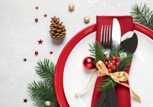 A festive table setting with a red plate, silverware wrapped in a red napkin, pine branches, berries, and decorative ornaments.
