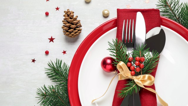 A festive table setting with a red plate, silverware wrapped in a red napkin, pine branches, berries, and decorative ornaments.