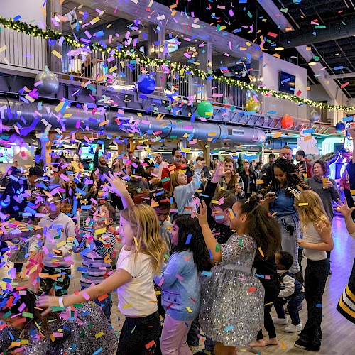 People celebrating indoors with colorful confetti and balloons, creating a festive atmosphere.
