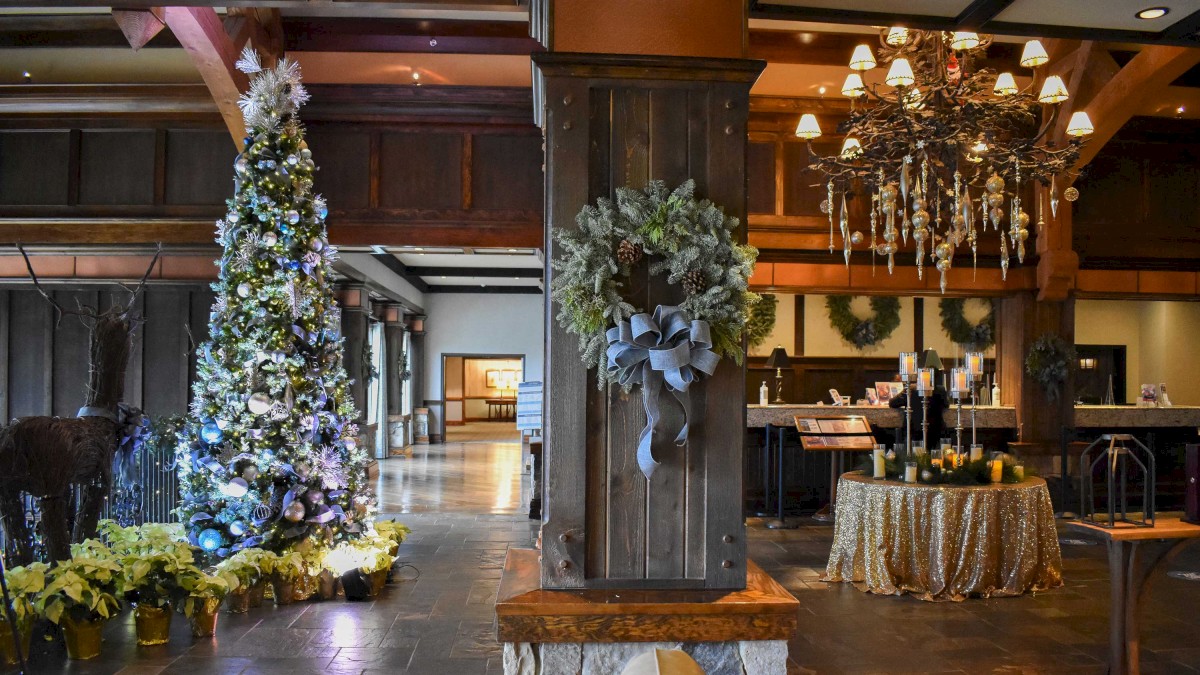 A festive interior with a decorated Christmas tree, wreath, elegant chandelier, and a draped table, creating a warm holiday ambiance.