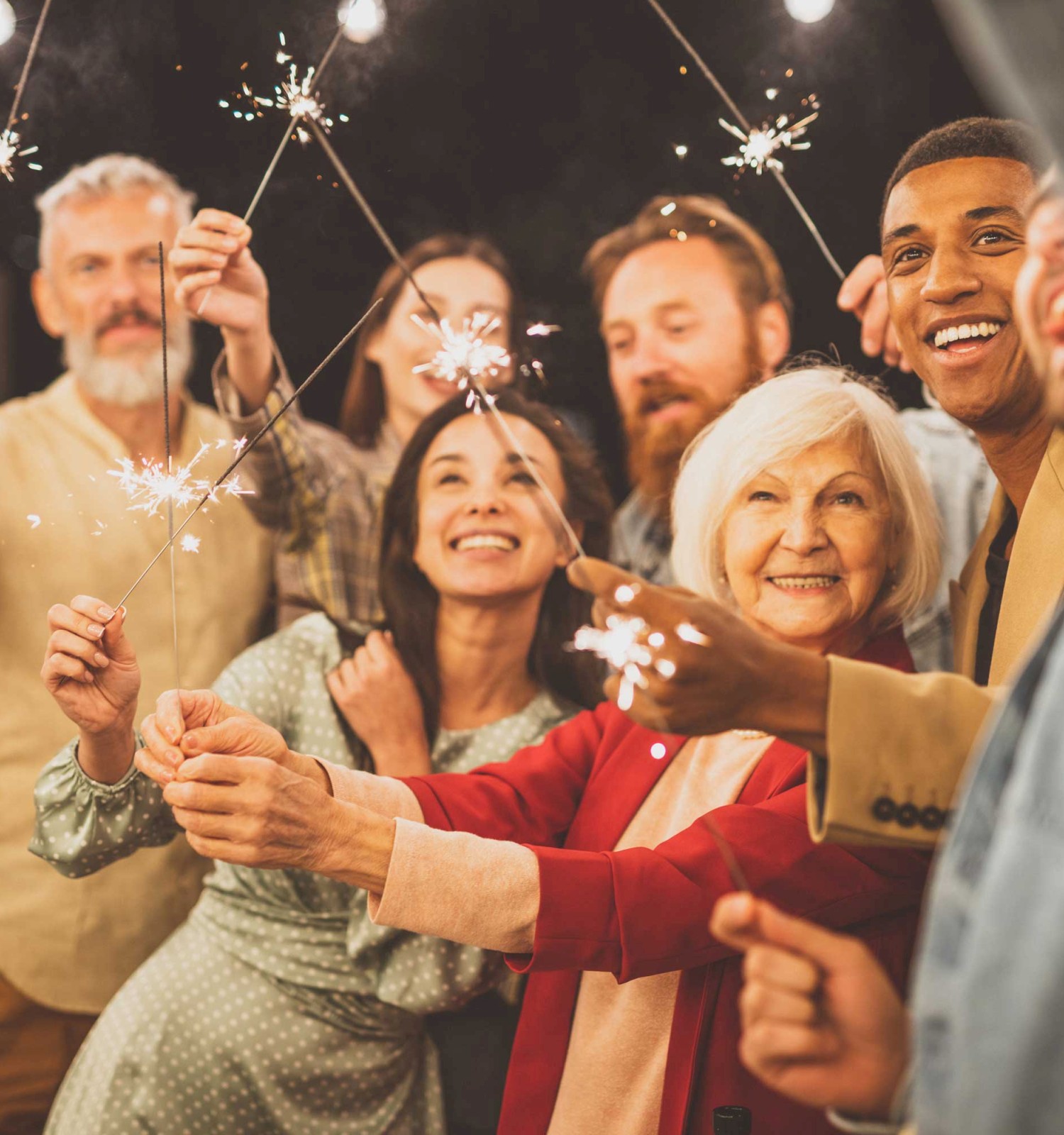 A diverse group of people are joyfully holding sparklers, celebrating together in a festive atmosphere, with warm expressions.