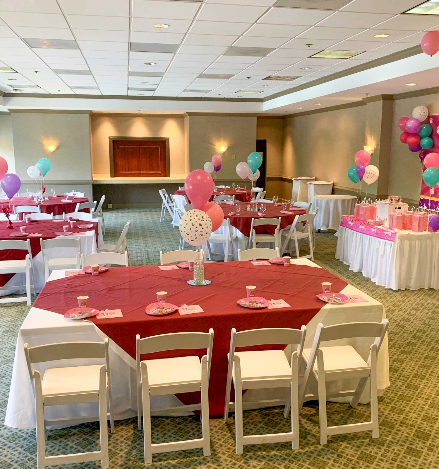 The image shows a decorated room for a birthday party with balloons, red tablecloths, and a 