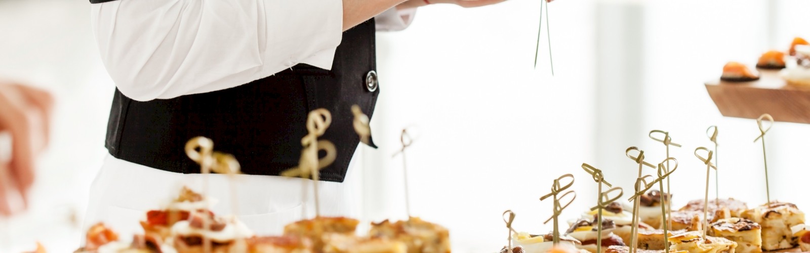 A person is arranging assorted appetizers on skewers at a catering event setup.