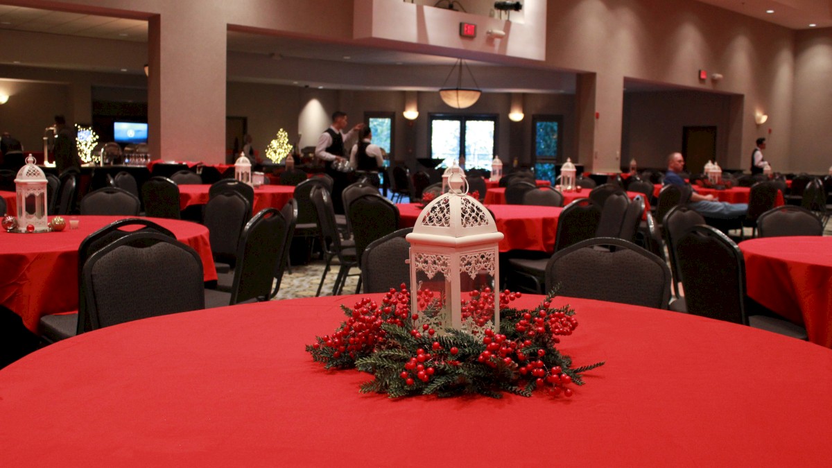 A decorated banquet hall with red-covered tables, centerpieces, and chairs set up for an event.