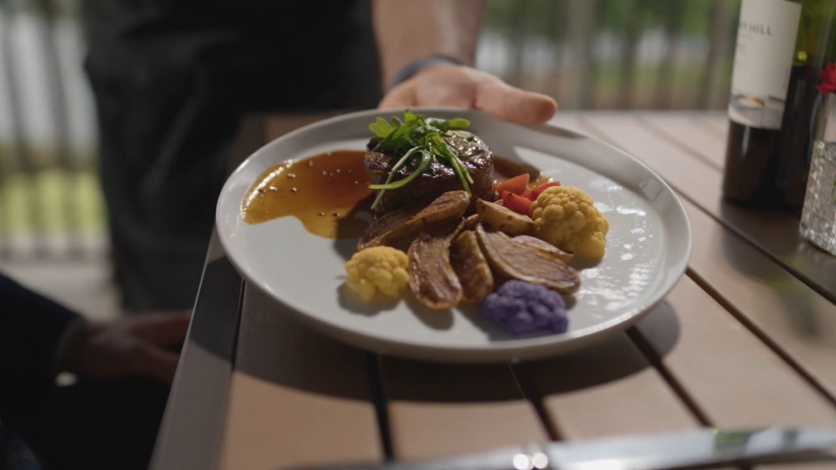A white plate with sliced meat, colorful cauliflower, sauce, and greens being served.