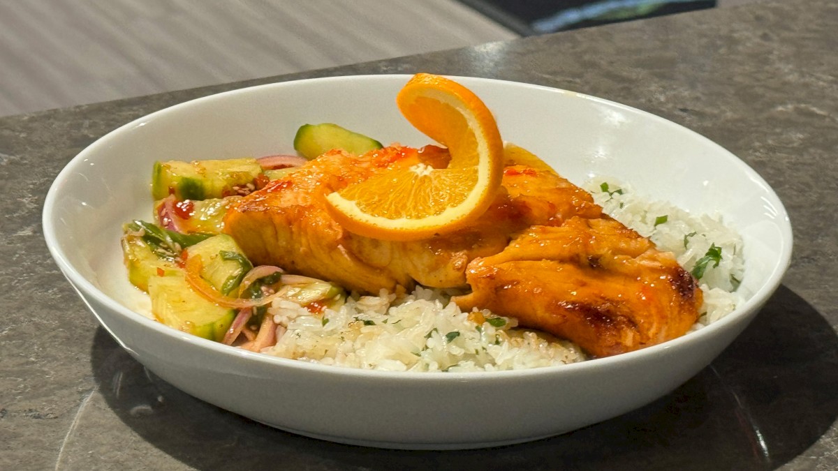 A bowl with cooked salmon on rice, garnished with orange slices and vegetables, placed on a countertop.