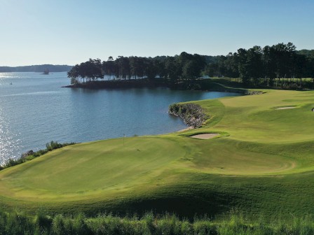 A beautiful lakeside golf course with lush greens, surrounded by trees and water under a clear blue sky.