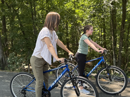 Two people are on blue bikes on a wooded path, enjoying a leisurely outdoor ride.