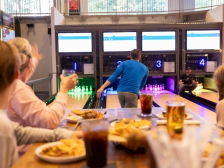 People are enjoying a meal and drinks while watching a game at a bowling alley.