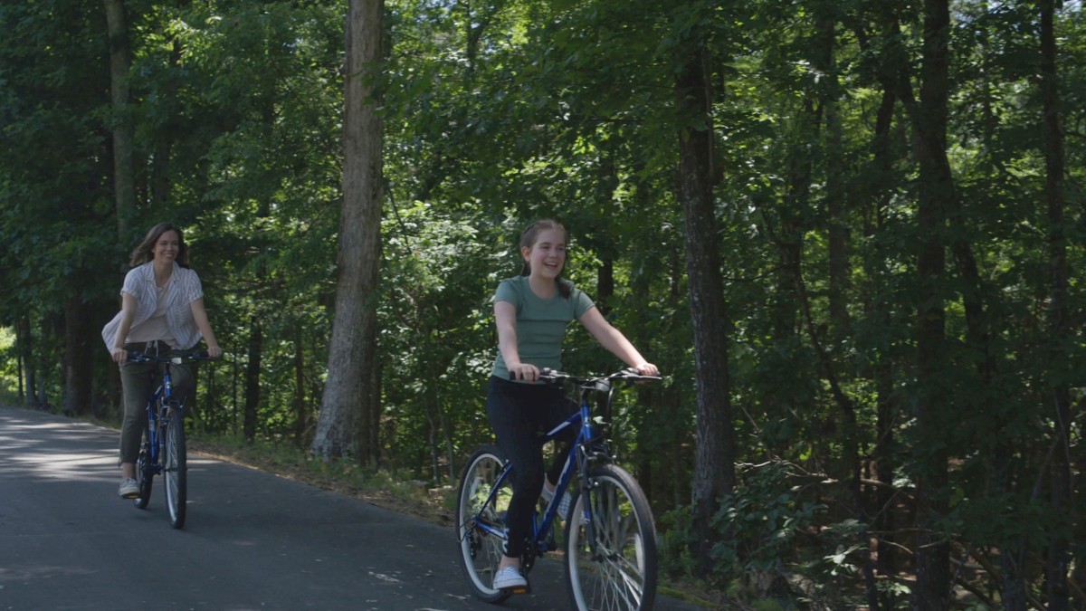 Two people are riding bicycles on a tree-lined road, enjoying a scenic outdoor setting.