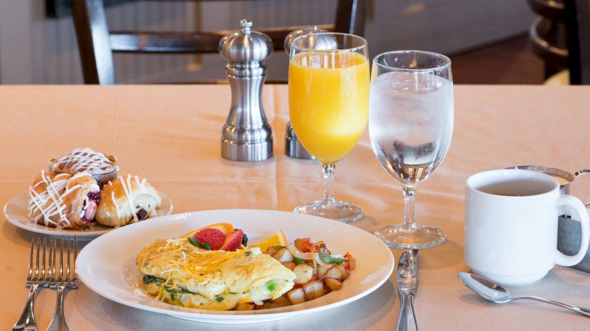 A breakfast setup with an omelette, pastries, orange juice, water, and coffee on a table, accompanied by cutlery and a pepper mill.