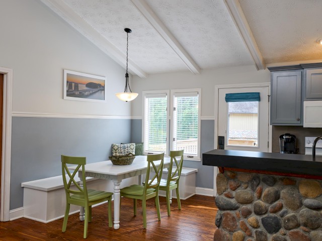 A kitchen with stone accent, green chairs at a white table, overhead light, and cabinets, featuring a cozy dining nook and decor.