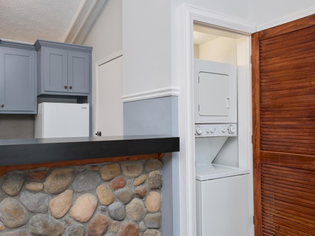 The image shows a kitchen area with grey cabinets, a stone-faced counter, and a white stacked washer-dryer unit in a small alcove.
