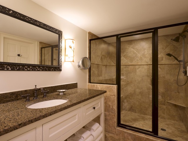 The image shows a bathroom with a granite countertop, a mirror, and a glass-enclosed shower area with tiled walls and floor.