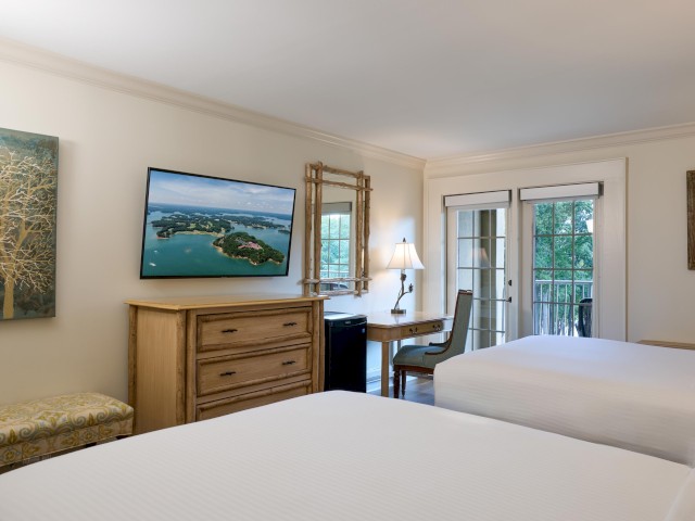 This image shows a hotel room with two beds, a desk, and a TV. There's an art piece and a window with a view outside.