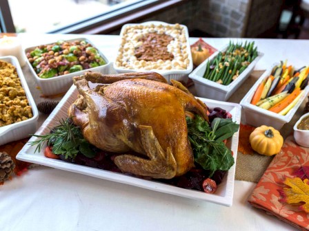 A roasted turkey is surrounded by various side dishes including stuffing, Brussels sprouts, green beans, mashed potatoes, and glazed carrots.