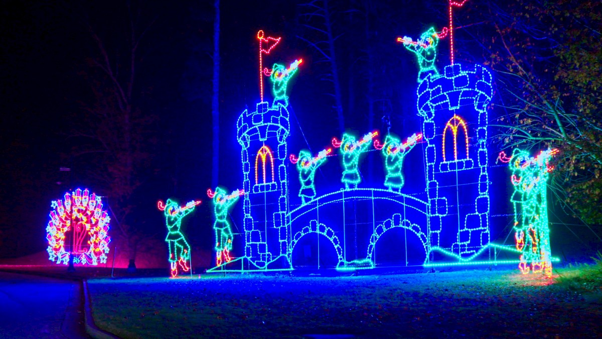 Colorful LED castle with knights on towers, a glowing archway, and a bright circular light display to the left, all shining at night.