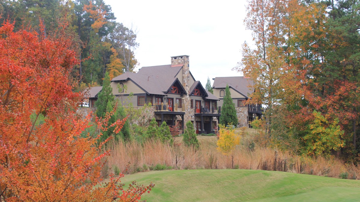 A large stone building is surrounded by colorful autumn trees and a grassy landscape, reflecting a serene and picturesque setting.