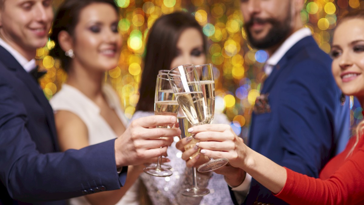 People in formal attire toast with champagne during a celebration, with colorful blurred lights in the background.