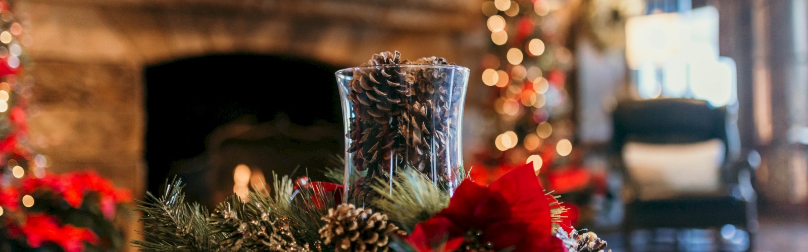 A festive room with a decorated fireplace, Christmas lights, and a pinecone centerpiece on a table, suggesting a cozy holiday setting.