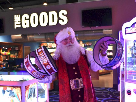 A person dressed as Santa in an arcade, holding large rolls of tickets, with a sign reading 