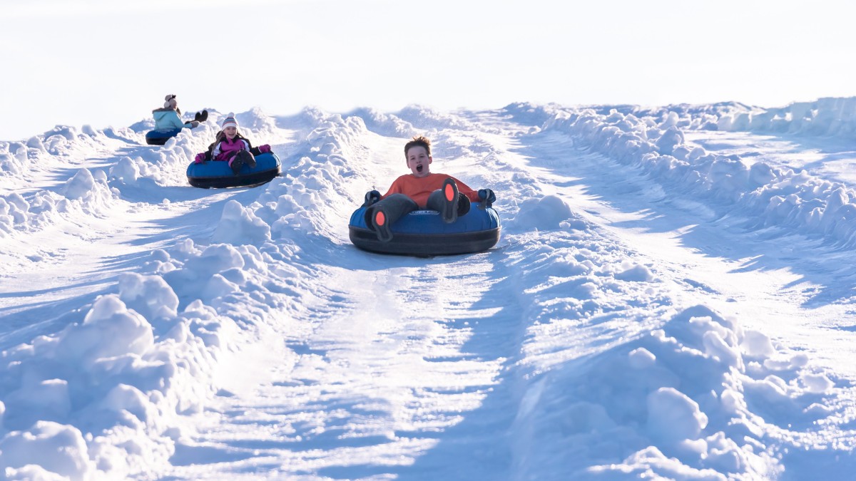 People are snow tubing down a snowy slope, enjoying the winter activity under a clear sky.