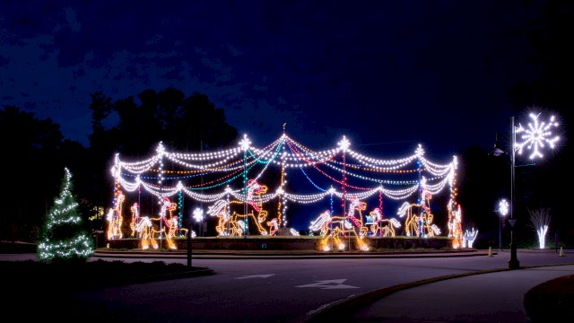 A carousel display with horse lights and colorful strings in a dark scene, accompanied by festive decorations and streetlights.
