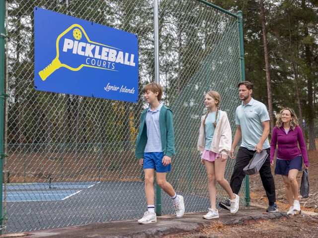 People walking past a Pickleball court sign at Lanier Islands, surrounded by trees and outdoor setting.
