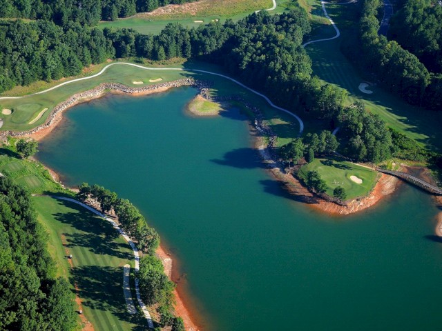 This is an aerial view of a golf course with a large lake, surrounded by trees and green fairways, showcasing a scenic landscape.