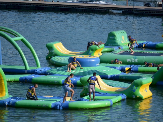 People are enjoying on a large inflatable water park with slides and climbing areas by the water.