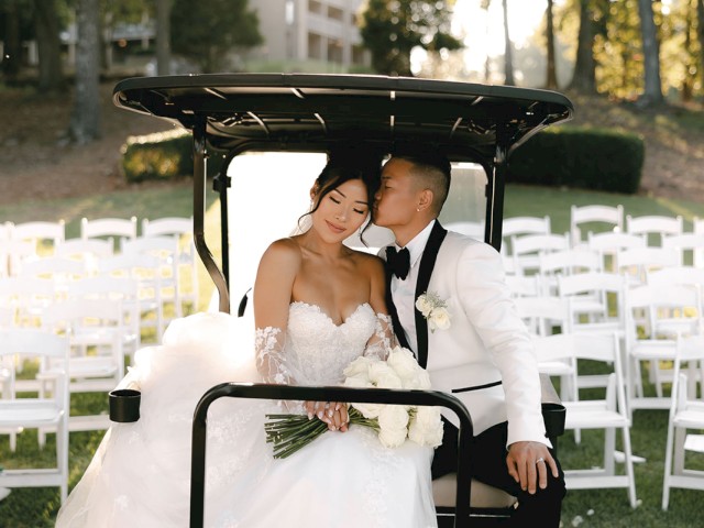 A bride and groom share a tender moment on a golf cart, surrounded by white chairs in an outdoor setting.