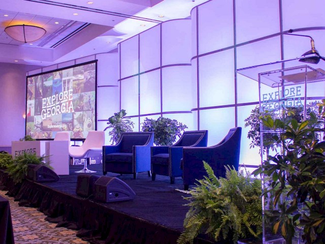 This image shows a conference room set up with chairs, a stage, a podium, and a large screen displaying 