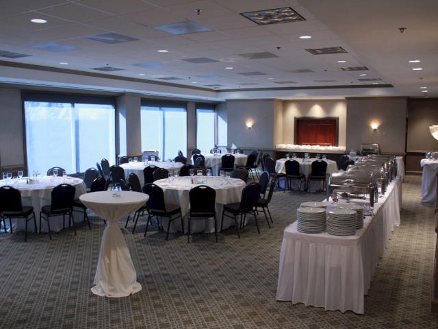 The image shows a banquet hall with arranged tables and chairs, buffet setup, and a high-top table, ready for an event or gathering.