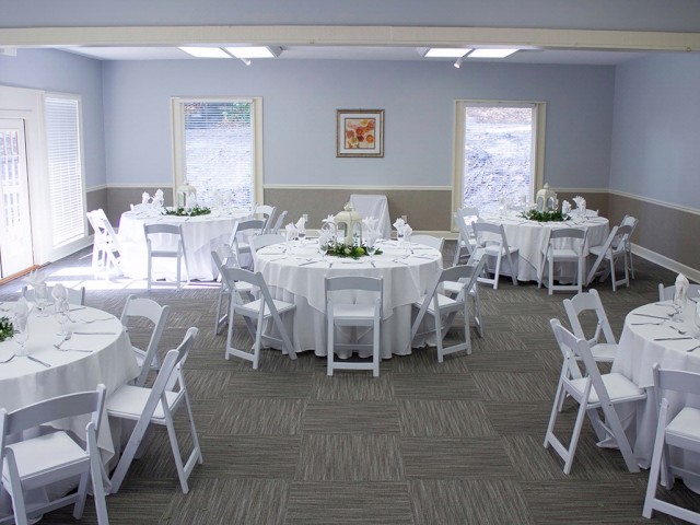 The image shows a banquet room with round tables covered in white linens and arranged with white chairs, ready for a formal event.