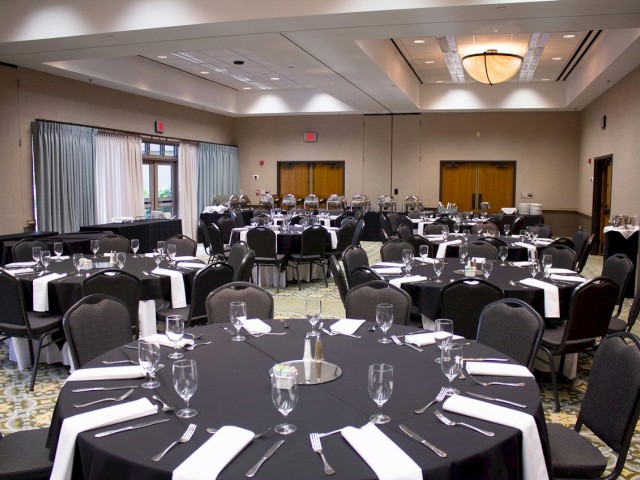 A banquet hall is set up for an event with round tables and chairs, each table arranged with silverware, glasses, and napkins.