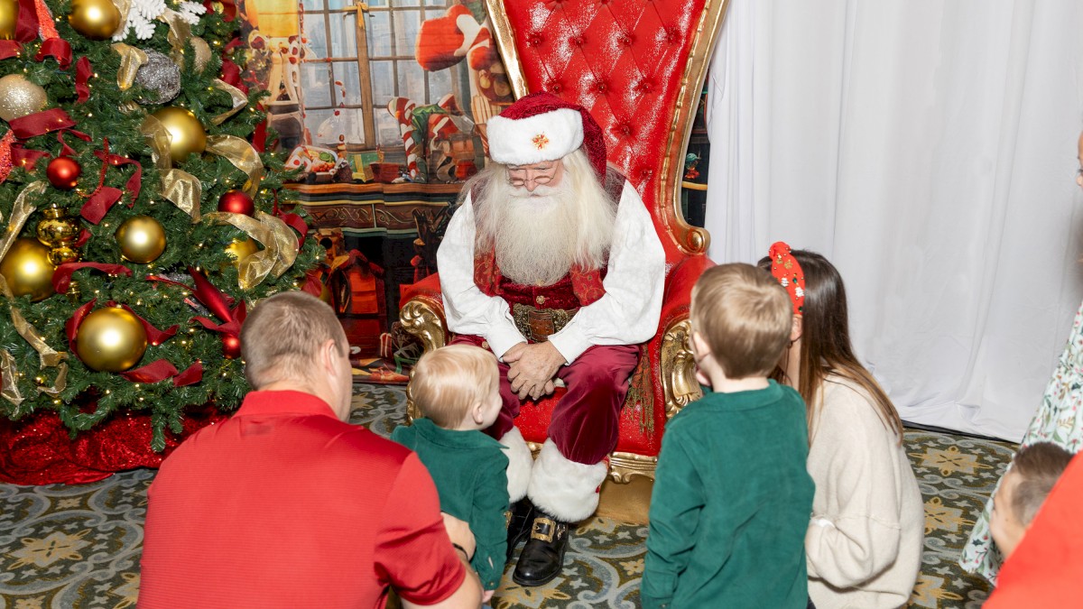 Santa Claus, a Christmas tree, and children sitting on the floor during a holiday event.