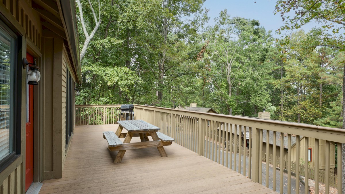 A spacious wooden deck with a picnic table overlooks a serene, leafy forest, providing a peaceful, nature-filled setting.